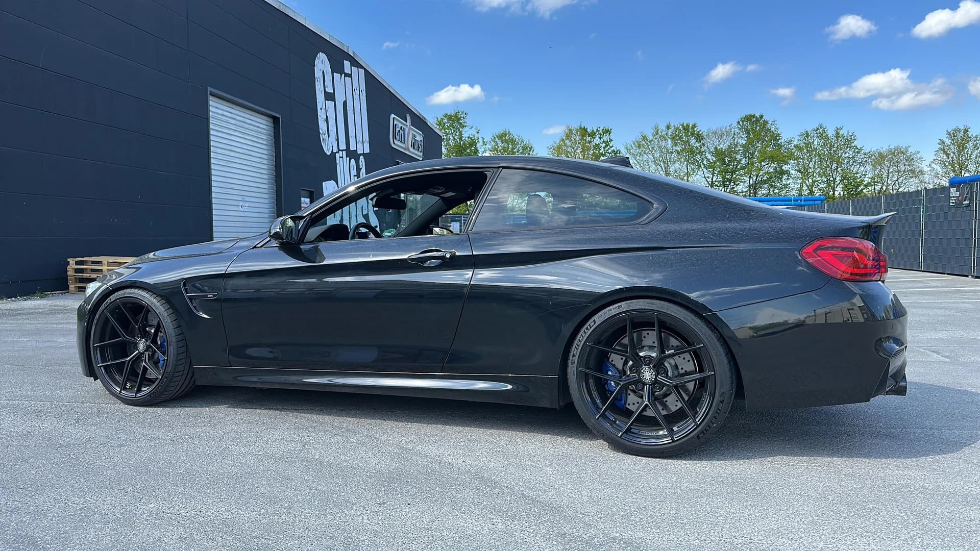 Dunkler BMW M4 in der Seitenansicht vor einer schwarzen Halle