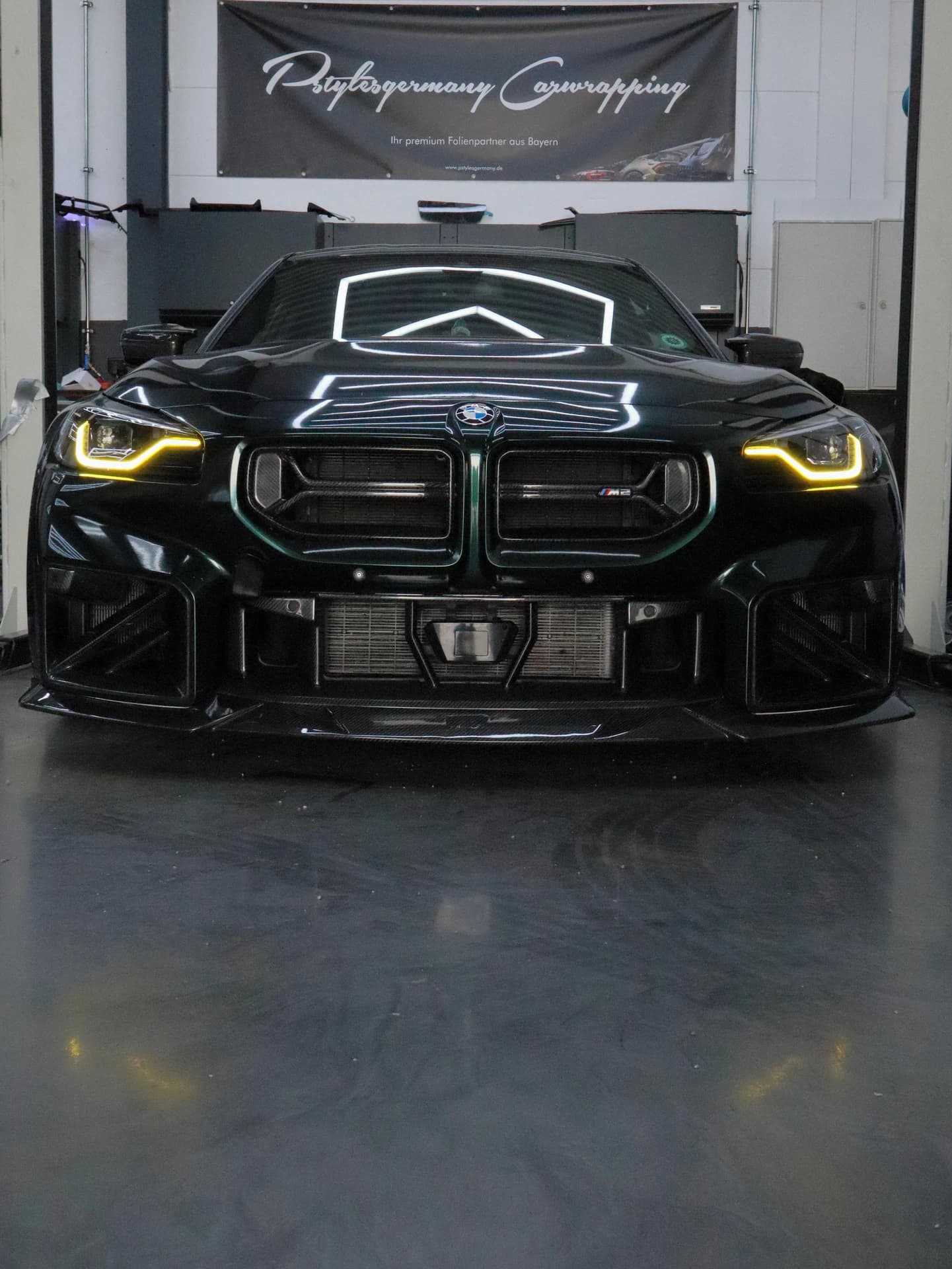 Schwarzer BMW M2 mit gelben Tagfahrlichtern frontal in der Halle