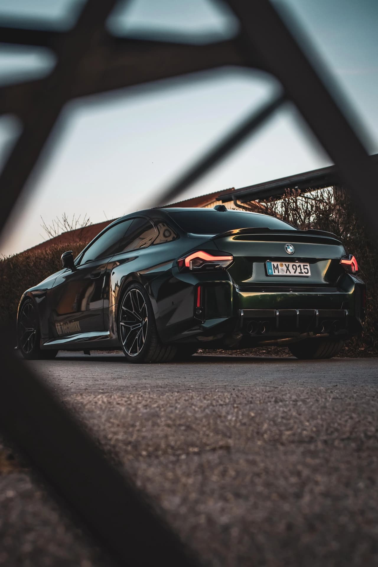 Schwarzer BMW M2 im Abendlicht, fotografiert durch ein Geländer hindurch