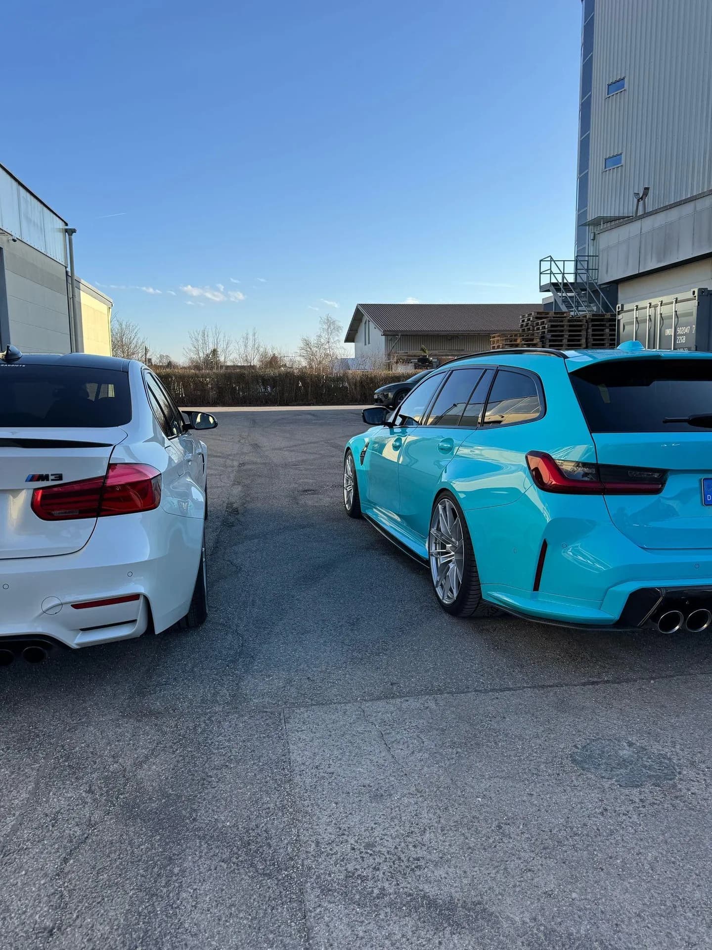 Weißer BMW M3 und türkisfarbener BMW M3 Touring nebeneinander auf dem Hof