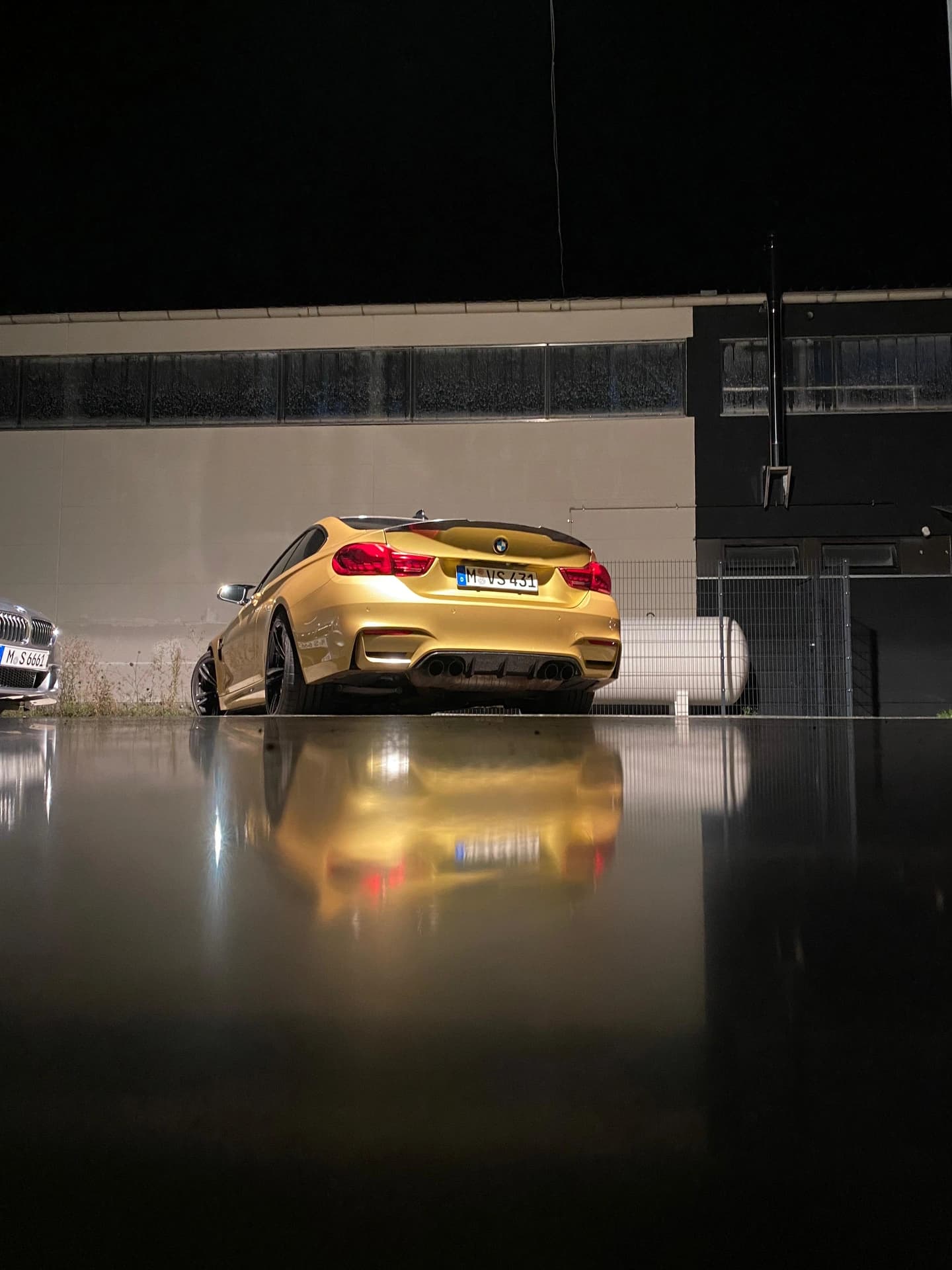 Goldfarbener BMW M4 bei Nacht vor der beleuchteten Werkstatthalle