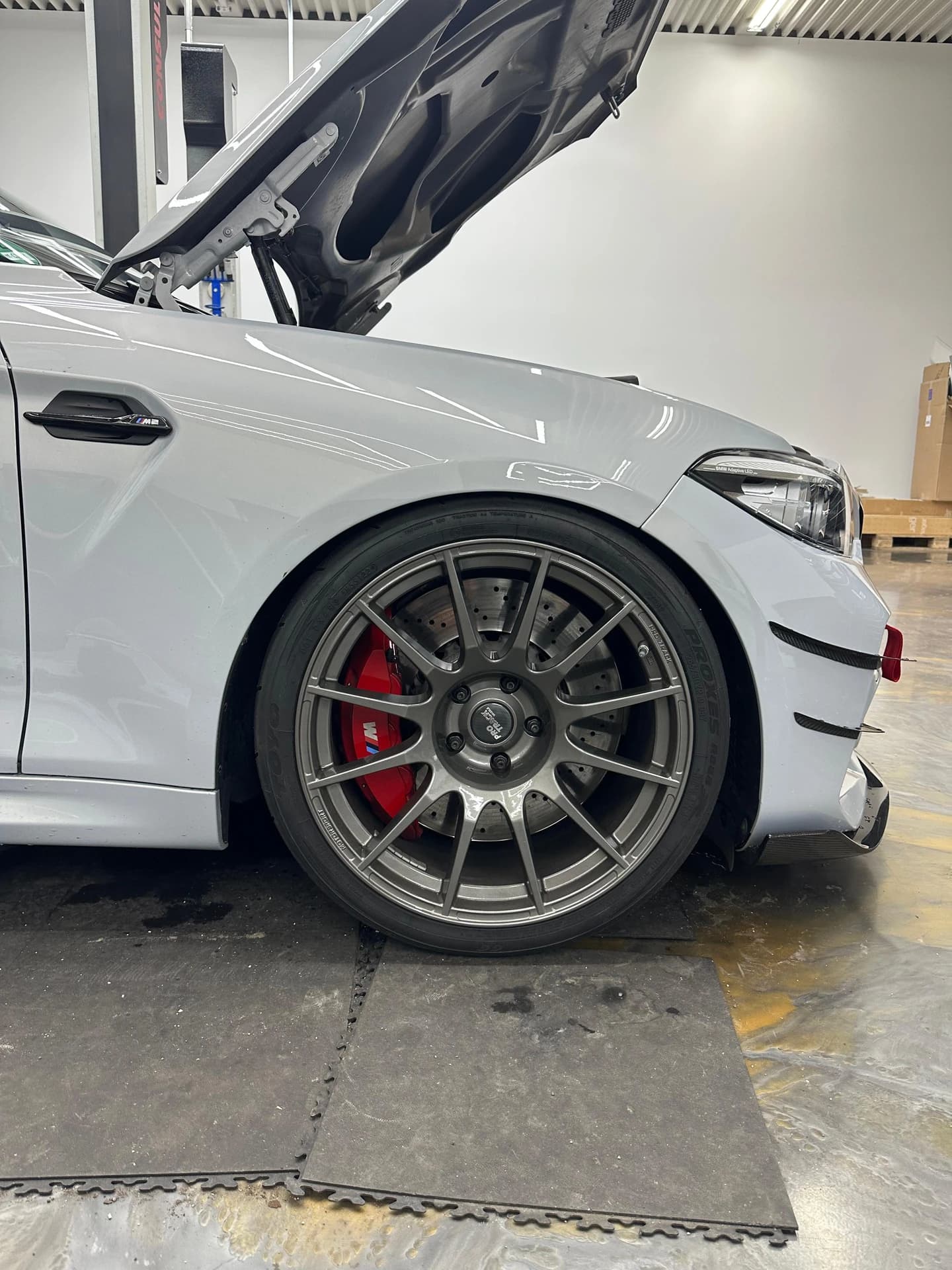 Grauer BMW M2 mit geöffneter Motorhaube in der Werkstatt