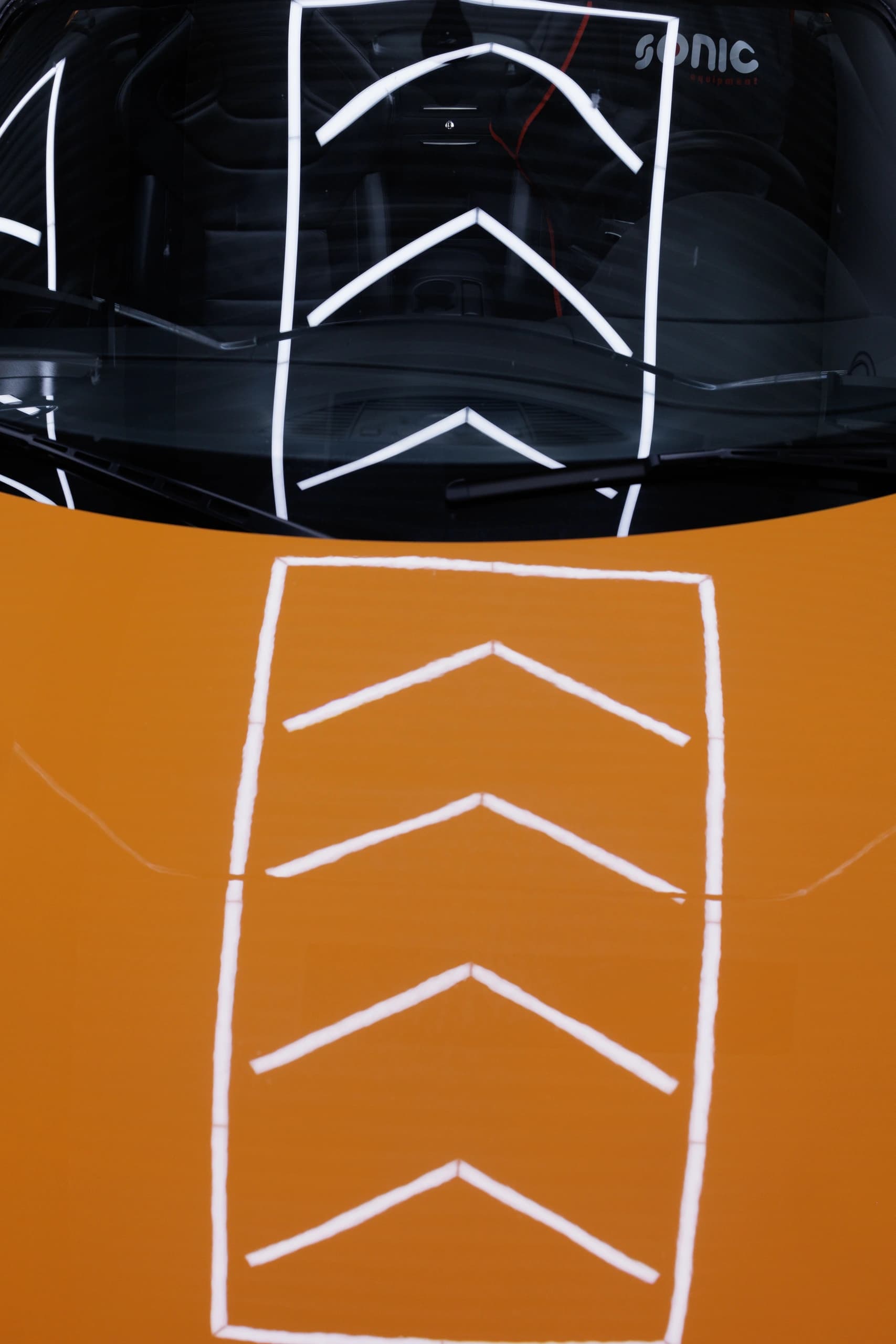 Die Deckenbeleuchtung der Werkstatt spiegelt sich auf einer orangefarbenen Motorhaube