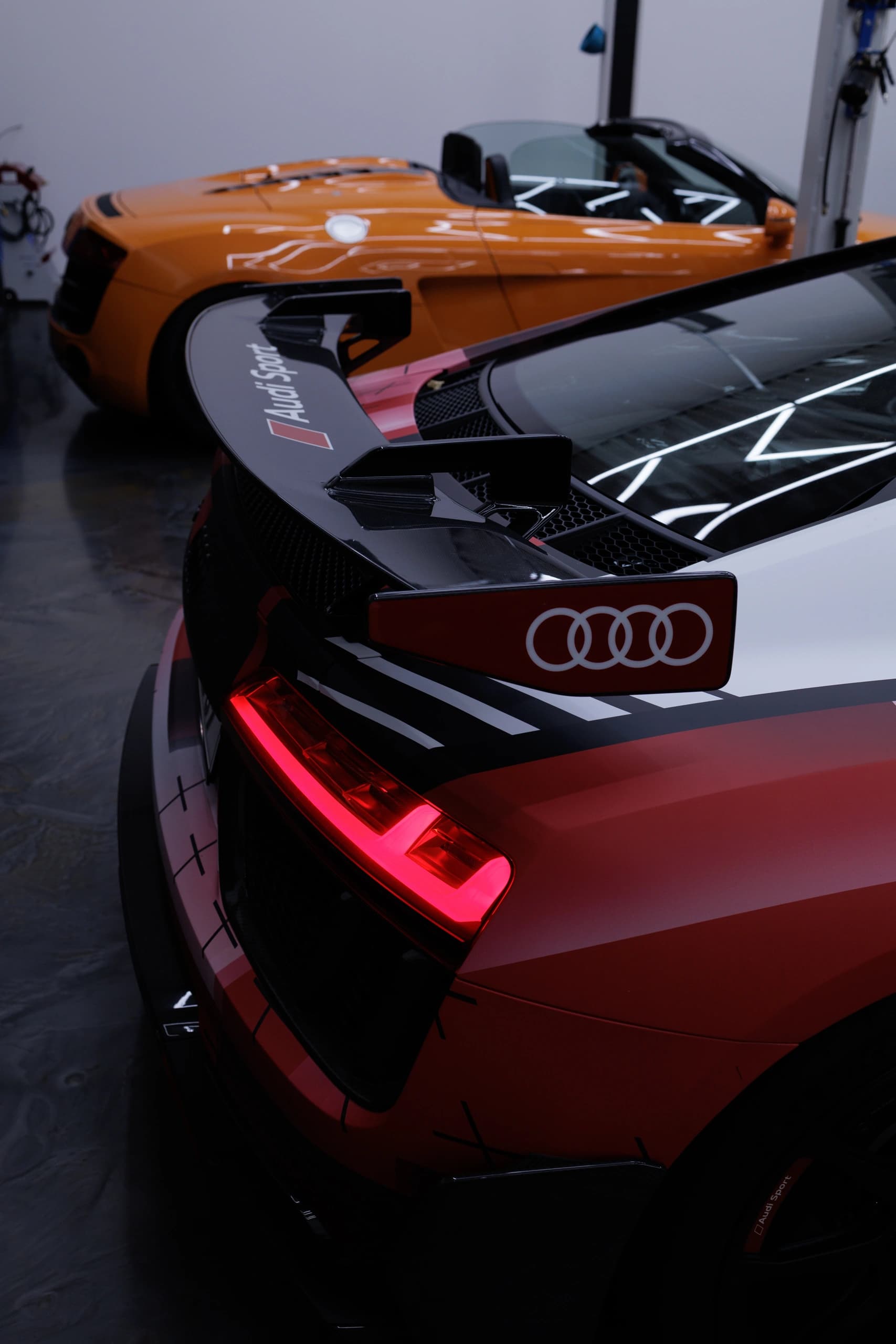 Heckflügel eines folierten Audi R8, dahinter ein orangefarbener Audi R8 Spyder