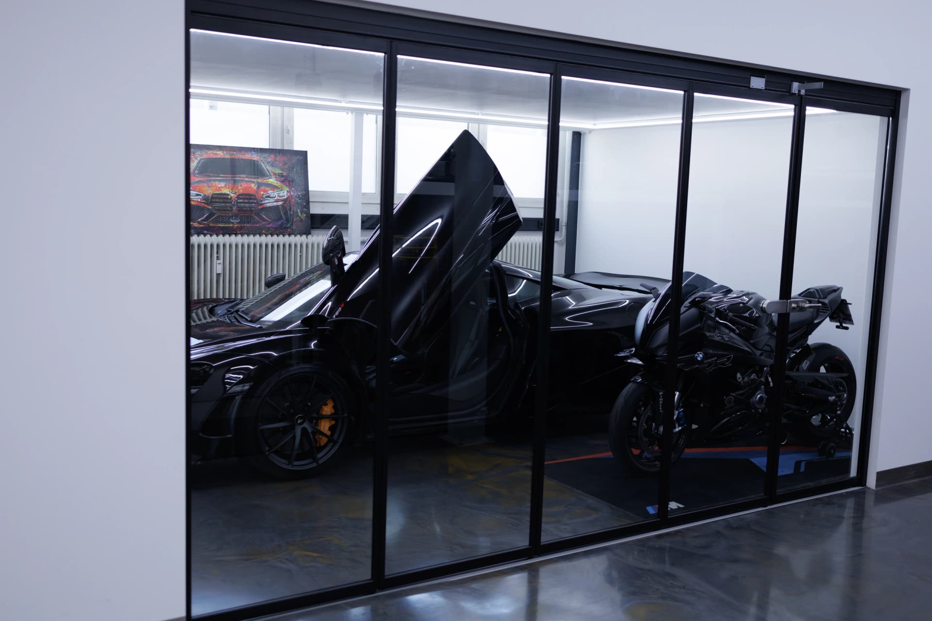 Schwarzer McLaren mit geöffneter Flügeltür und eine BMW S1000RR im verglasten Showroom