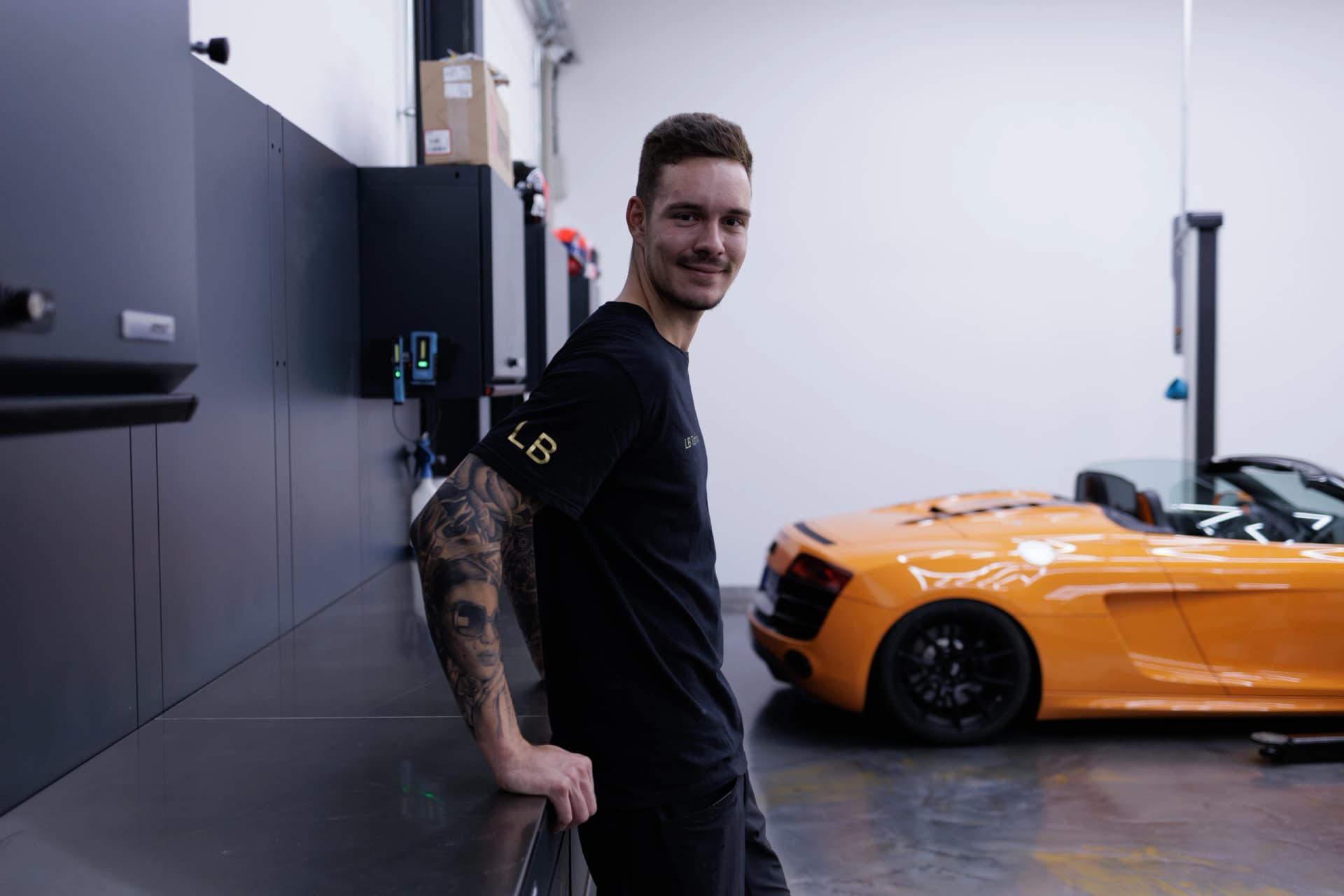 Leon an der Werkbank, im Hintergrund ein orangefarbener Audi R8 Spyder